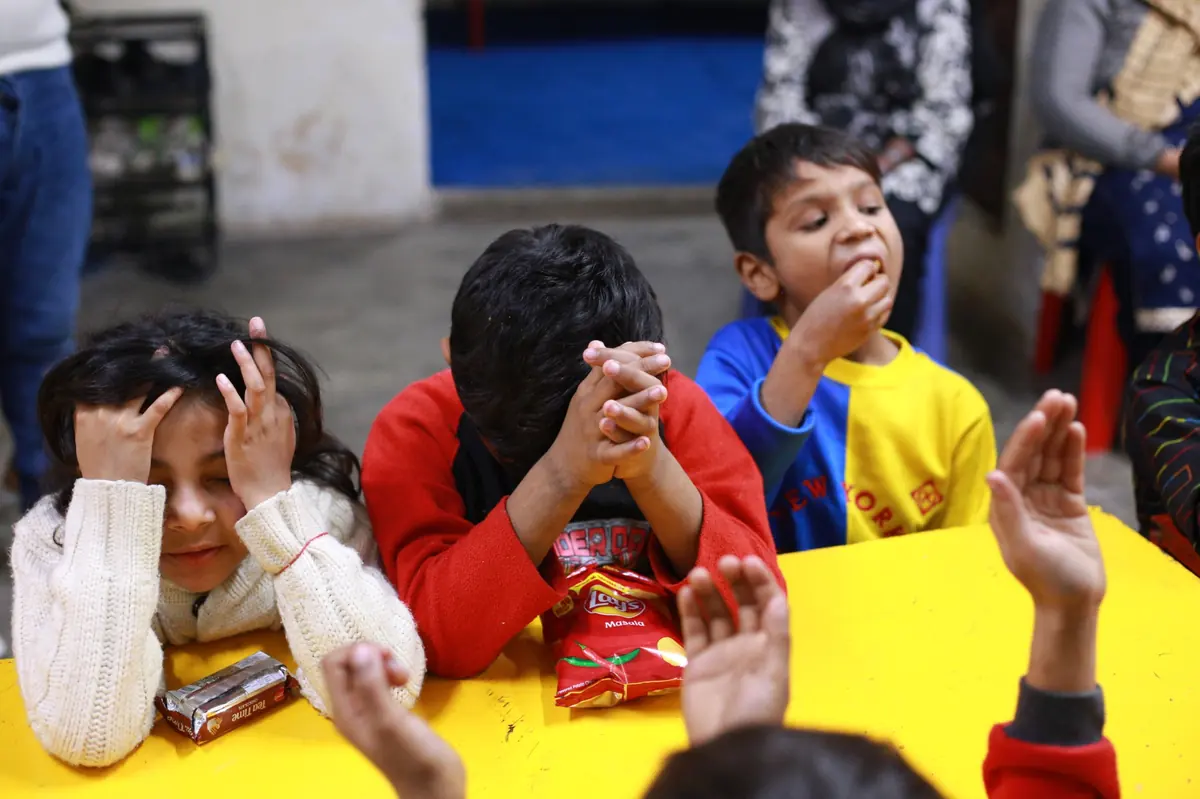 Children with hands folded in prayer around a table before receiving their meal and gifts