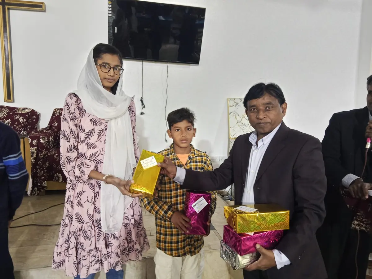 A pastor and a helper presenting wrapped gift parcels to a boy at a church programme