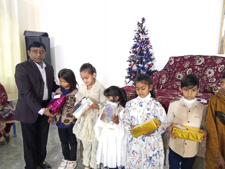 A pastor handing wrapped gifts to small children beside a Christmas tree in church