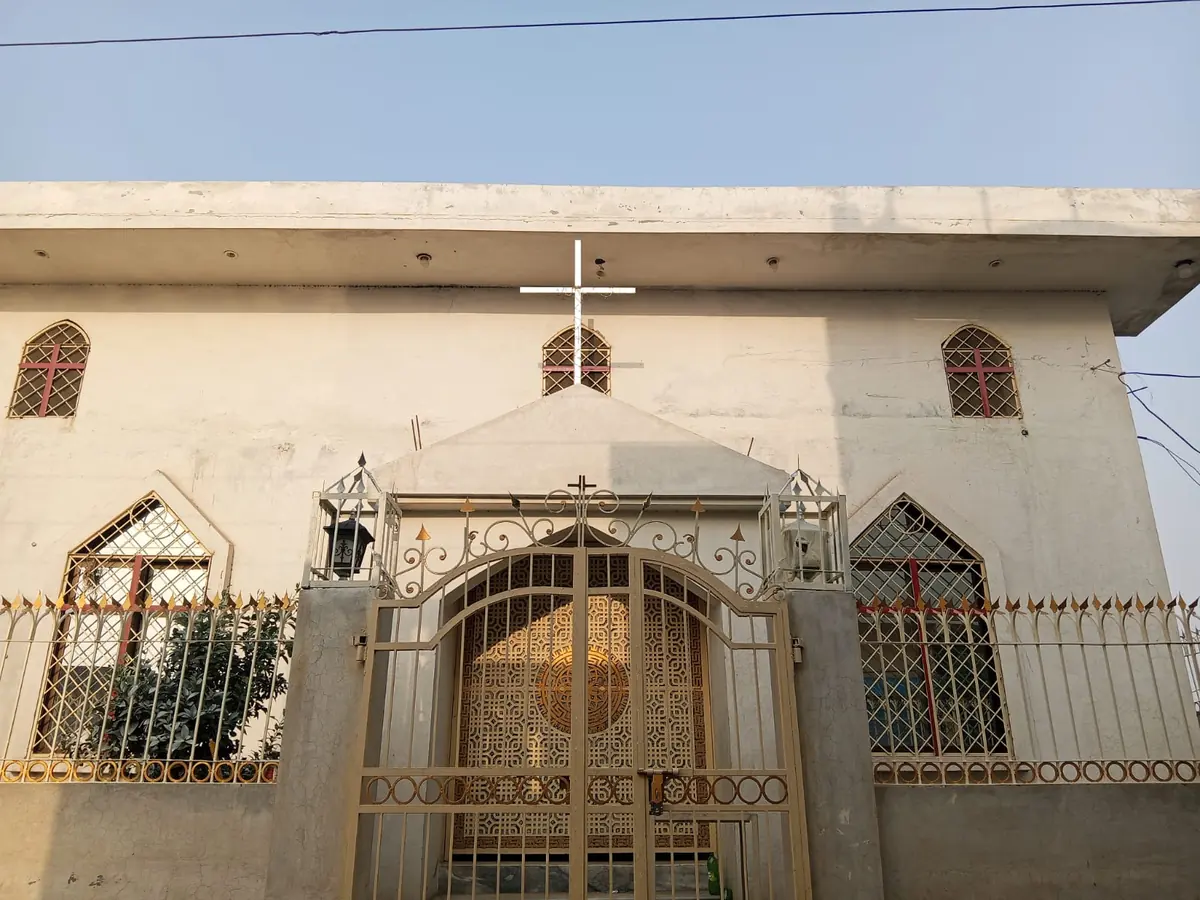 The gated front entrance of a Pakistani church building with a cross above the doorway