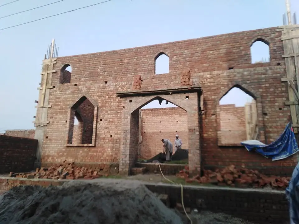 An unfinished brick church building with open arched windows awaiting a roof and plaster