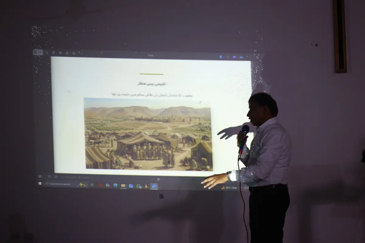 A ministry worker speaking into a microphone beside a projected teaching slide