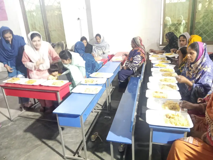 Women and children seated at long tables with plates of hot food during a community meal