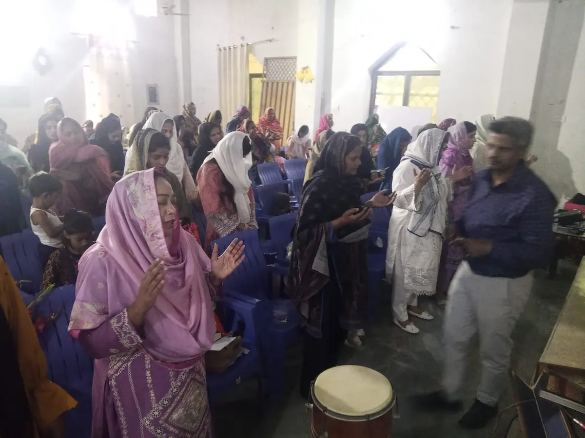 A congregation of Pakistani women standing with hands folded in prayer