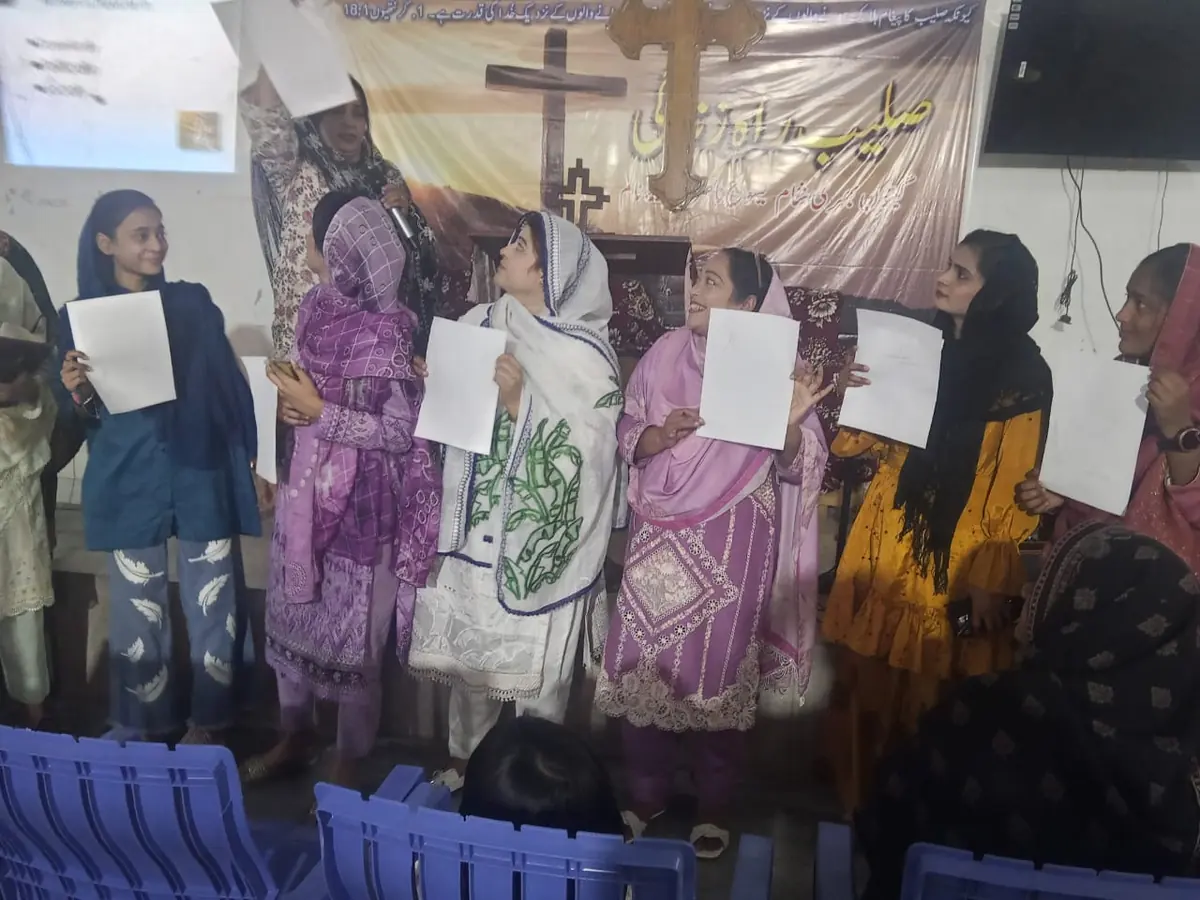 Women holding Scripture worksheets during a church teaching session beneath a cross